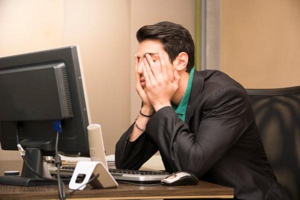 Frustrated man at computer with hands over face 